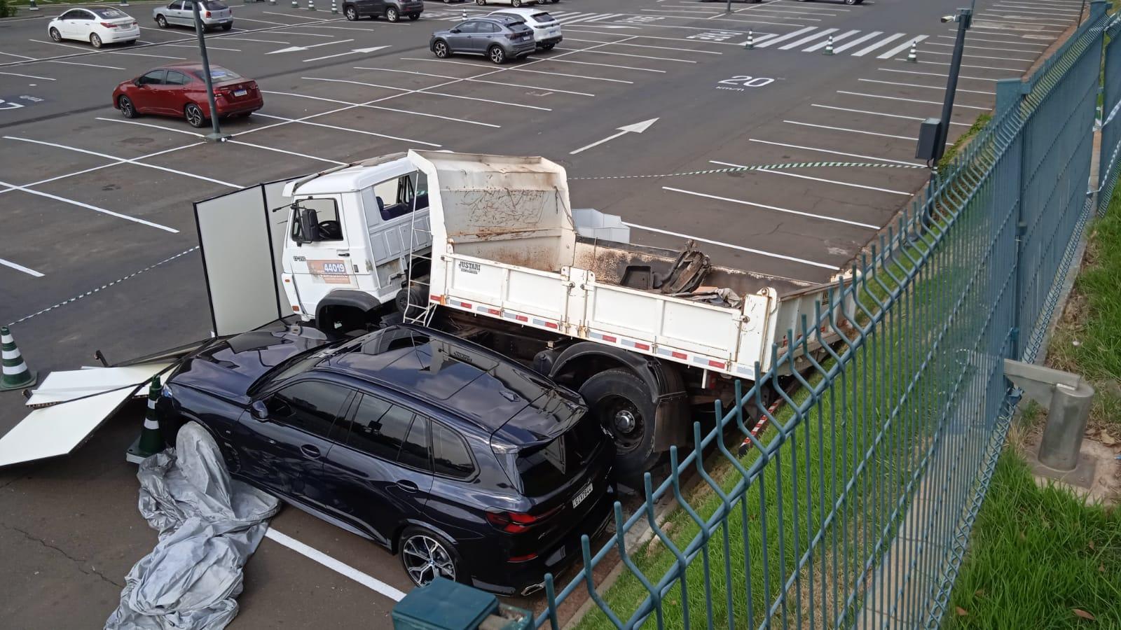 Caminhão desgovernado atravessa avenida, cai em estacionamento de shopping e atinge BMW